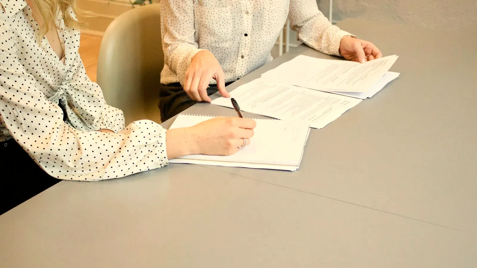 Deux mains autour d’un dossier sur une table : l’une écrit, l’autre est posée à côté en soutien