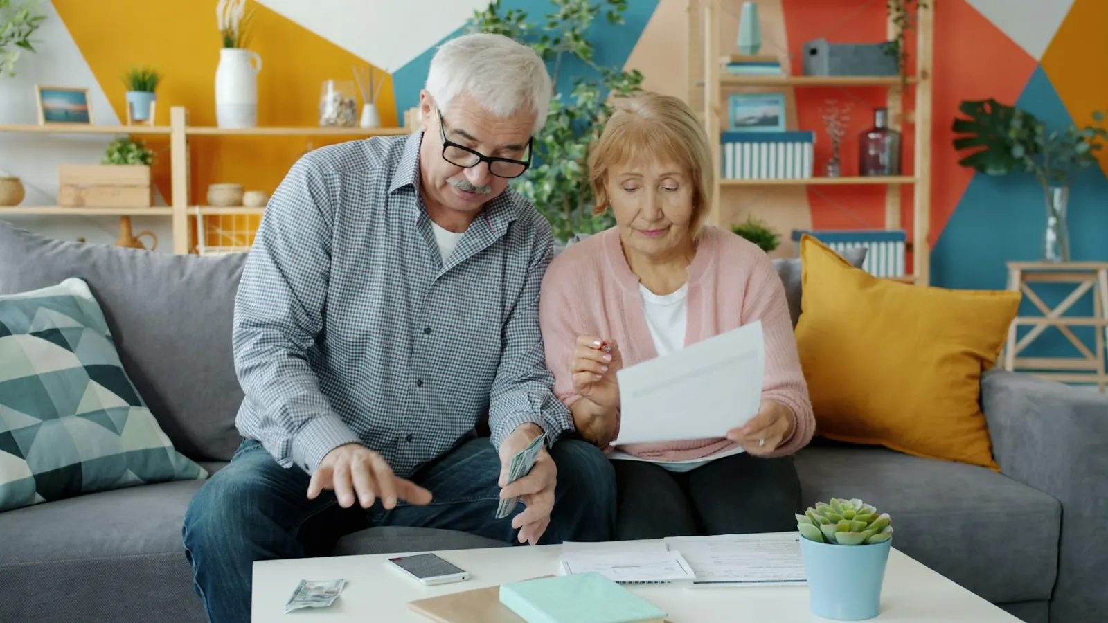 Couple de seniors souriants remplissant des papiers dans leur salon